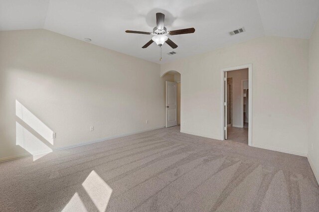 carpeted empty room featuring arched walkways, a ceiling fan, visible vents, and vaulted ceiling