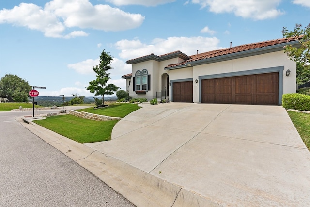 mediterranean / spanish-style home featuring a tile roof, a front yard, concrete driveway, an attached garage, and stucco siding