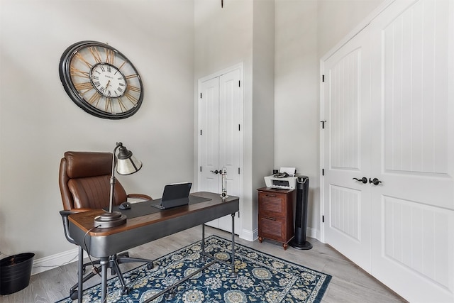 home office with baseboards, light wood finished floors, and a towering ceiling