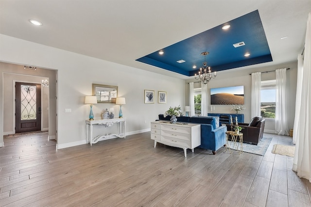 living area with a raised ceiling, wood finished floors, and a chandelier