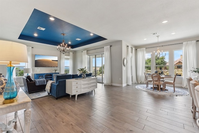 living area with a raised ceiling, a glass covered fireplace, wood finished floors, and a chandelier