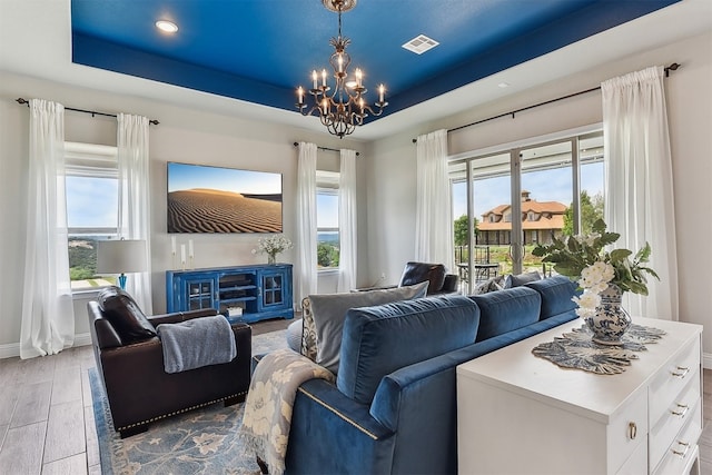 living area with an inviting chandelier, recessed lighting, baseboards, a tray ceiling, and visible vents