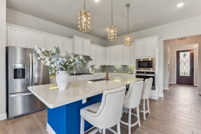 kitchen featuring a kitchen breakfast bar, backsplash, a sink, light wood-style floors, and stainless steel appliances