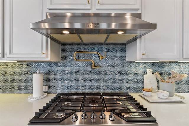 interior details featuring light countertops, white cabinetry, decorative backsplash, stainless steel gas stovetop, and range hood