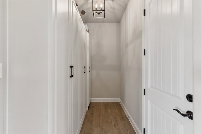 hall with baseboards, a notable chandelier, and wood finished floors