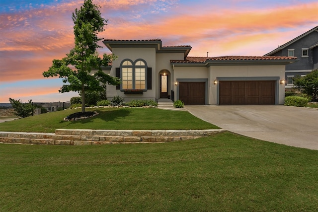 mediterranean / spanish house with an attached garage, stucco siding, a lawn, a tiled roof, and driveway