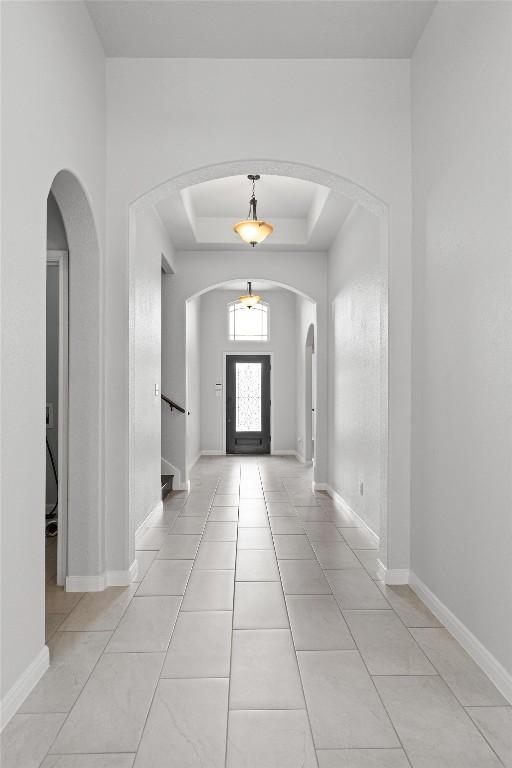 entryway with arched walkways, light tile patterned floors, baseboards, a raised ceiling, and stairs