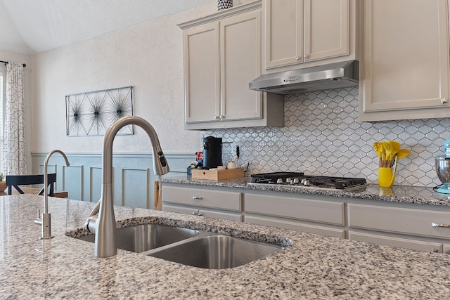 kitchen featuring stainless steel gas cooktop, lofted ceiling, under cabinet range hood, tasteful backsplash, and a sink