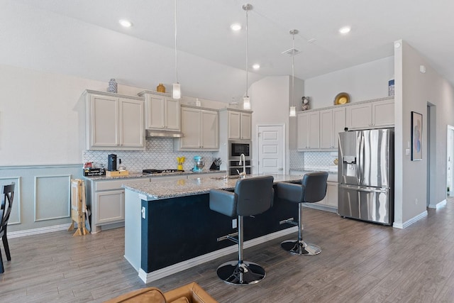 kitchen featuring a kitchen island with sink, appliances with stainless steel finishes, tasteful backsplash, a sink, and light wood-style floors
