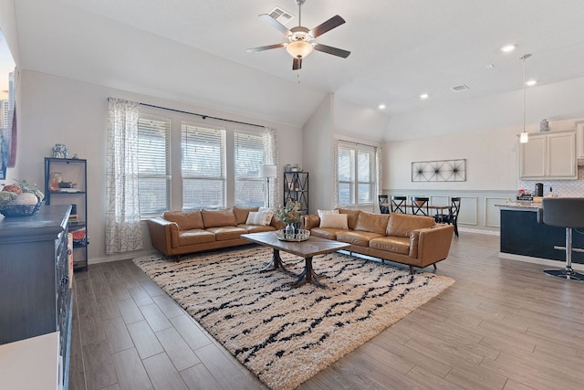 living area featuring light wood-style floors, a ceiling fan, vaulted ceiling, and visible vents