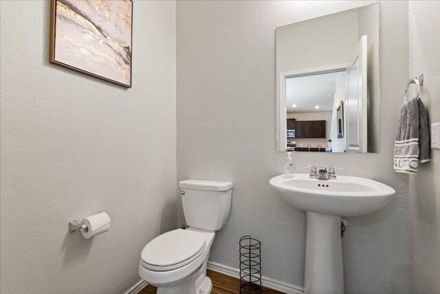 half bath with toilet, baseboards, a sink, and wood finished floors