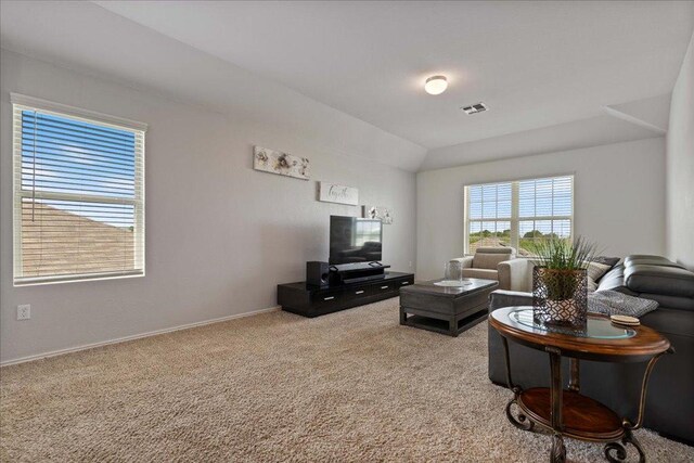 carpeted living area featuring baseboards, visible vents, and lofted ceiling