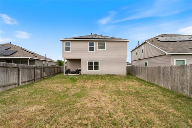 back of house with a fenced backyard, a lawn, and solar panels