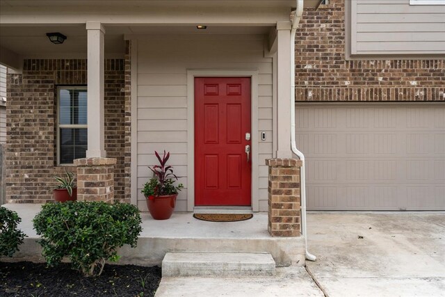 doorway to property featuring brick siding, a garage, and covered porch