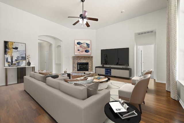 living area with ceiling fan, arched walkways, a fireplace, wood finished floors, and baseboards