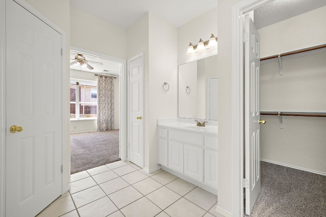 bathroom with vanity, tile patterned flooring, baseboards, a walk in closet, and a ceiling fan