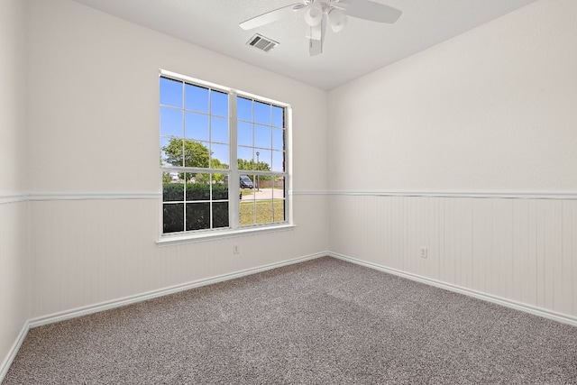 spare room with carpet floors, a ceiling fan, visible vents, and a wainscoted wall
