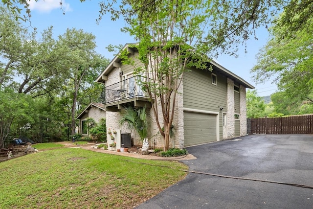 view of property exterior with fence, a balcony, aphalt driveway, a yard, and an attached garage