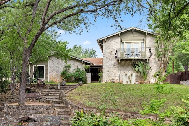back of house with fence, stone siding, a yard, and a balcony