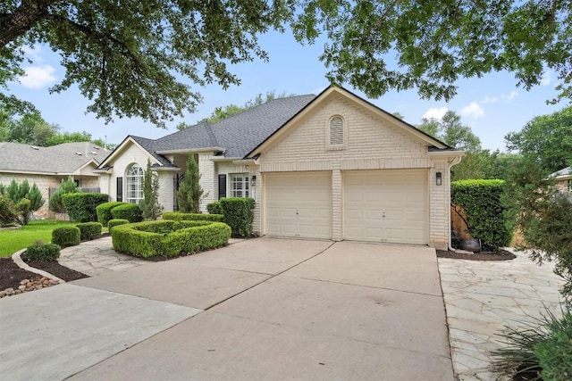 ranch-style house with an attached garage, roof with shingles, driveway, and brick siding