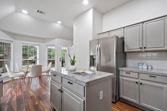 kitchen featuring light countertops, a kitchen island, stainless steel refrigerator with ice dispenser, visible vents, and dark wood-style floors