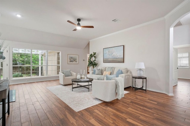 living area featuring dark wood-type flooring, a ceiling fan, arched walkways, and ornamental molding