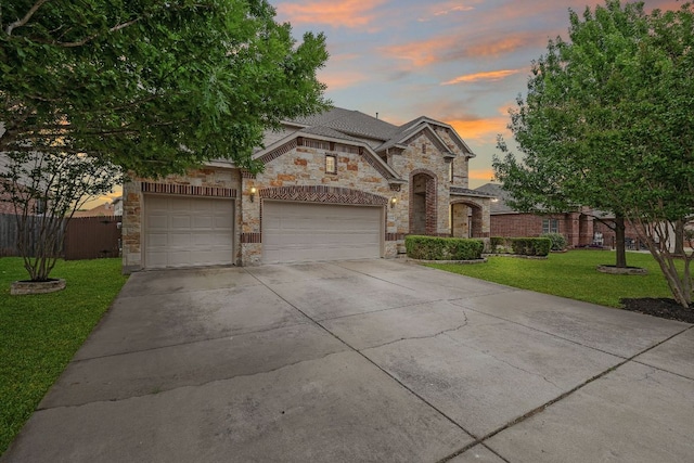 french country home featuring fence, stone siding, a garage, a lawn, and driveway
