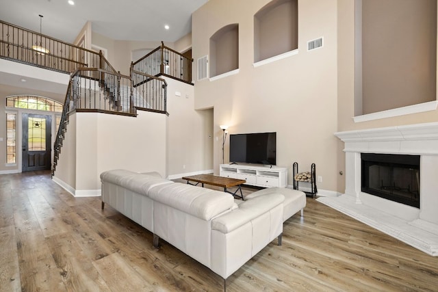 living area featuring stairway, a high ceiling, wood finished floors, and visible vents