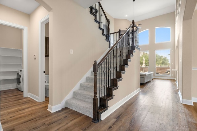 stairway featuring washer / dryer, wood finished floors, baseboards, a high ceiling, and arched walkways