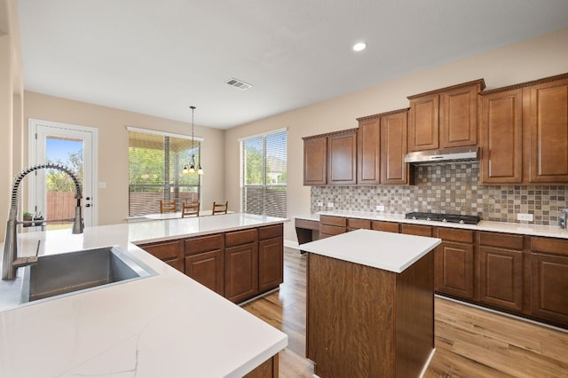 kitchen featuring stainless steel gas cooktop, a center island, under cabinet range hood, a sink, and light wood-style flooring
