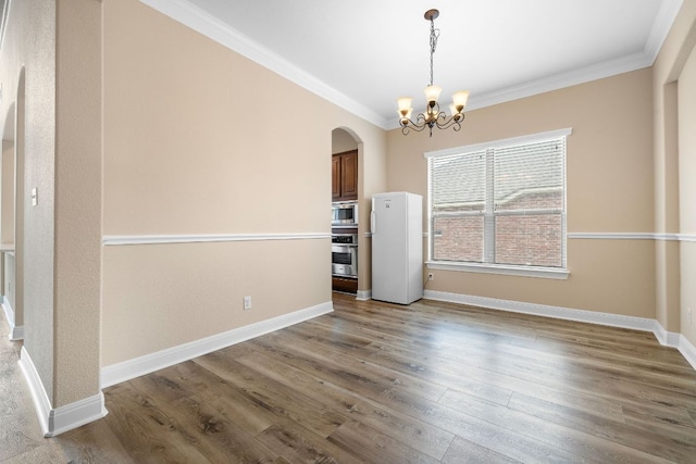 unfurnished dining area with crown molding, arched walkways, wood finished floors, and an inviting chandelier