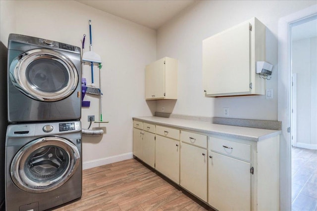 clothes washing area with baseboards, cabinet space, stacked washing maching and dryer, and light wood finished floors