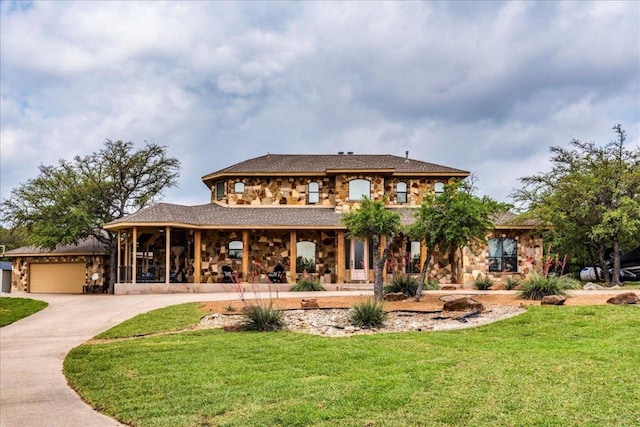 rear view of house featuring an attached garage, a yard, stone siding, and concrete driveway