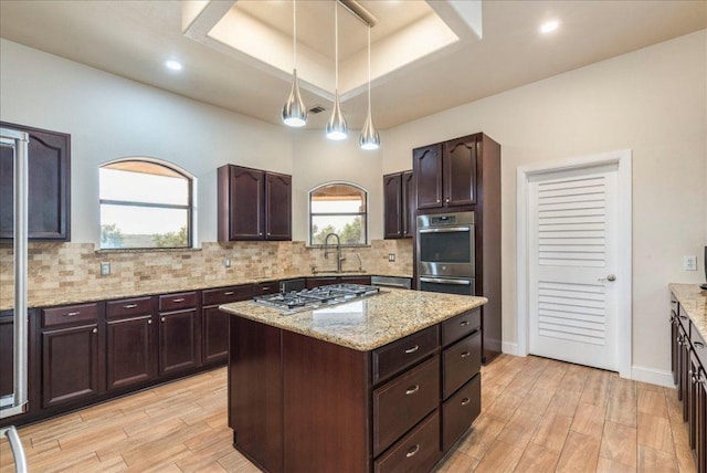 kitchen with light stone counters, stainless steel gas cooktop, light wood-style flooring, backsplash, and a tray ceiling