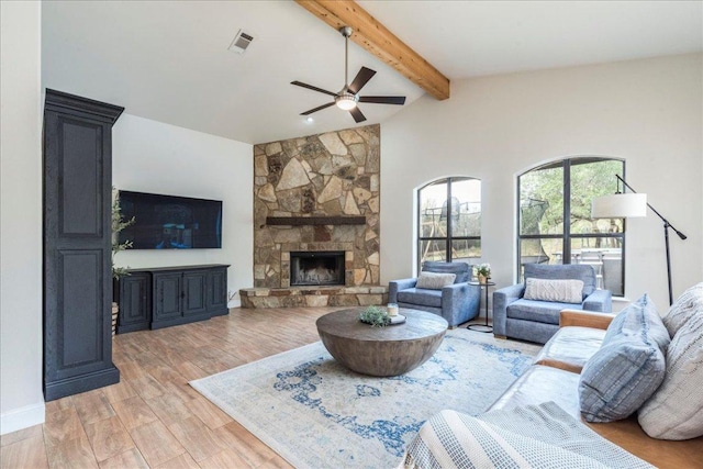 living area with ceiling fan, a stone fireplace, vaulted ceiling with beams, light wood-type flooring, and visible vents