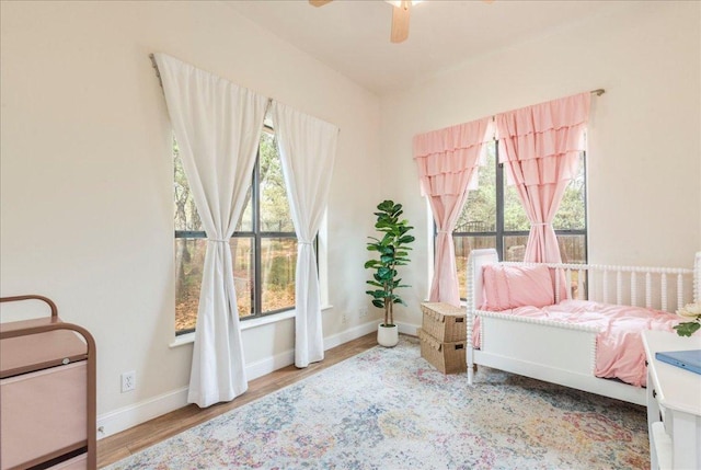 bedroom featuring baseboards, ceiling fan, wood finished floors, and multiple windows