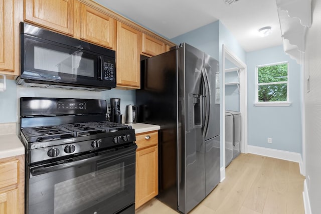 kitchen with baseboards, light countertops, washing machine and clothes dryer, light wood finished floors, and black appliances