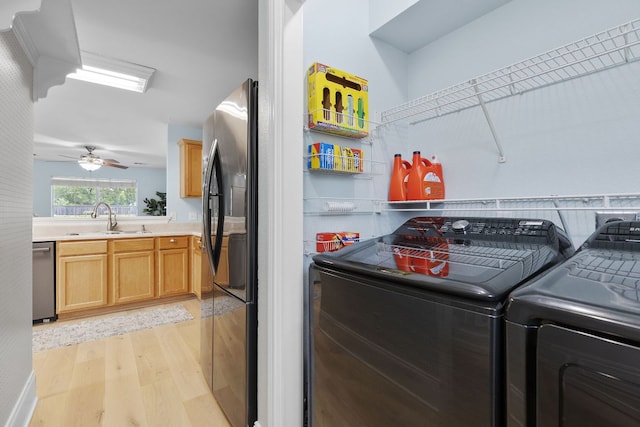 laundry area with laundry area, a ceiling fan, washer and clothes dryer, a sink, and light wood finished floors