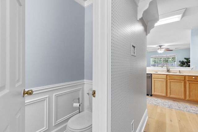 bathroom featuring a sink, double vanity, toilet, a wainscoted wall, and wood finished floors