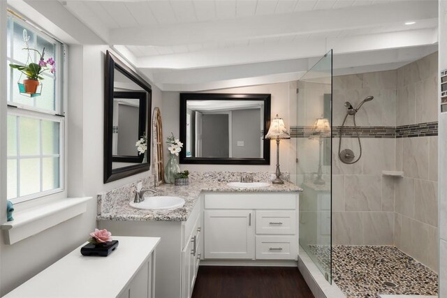 full bath featuring double vanity, wood finished floors, a sink, a walk in shower, and beamed ceiling