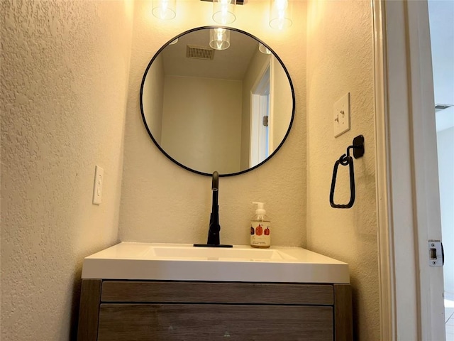 bathroom featuring vanity, a textured wall, and visible vents