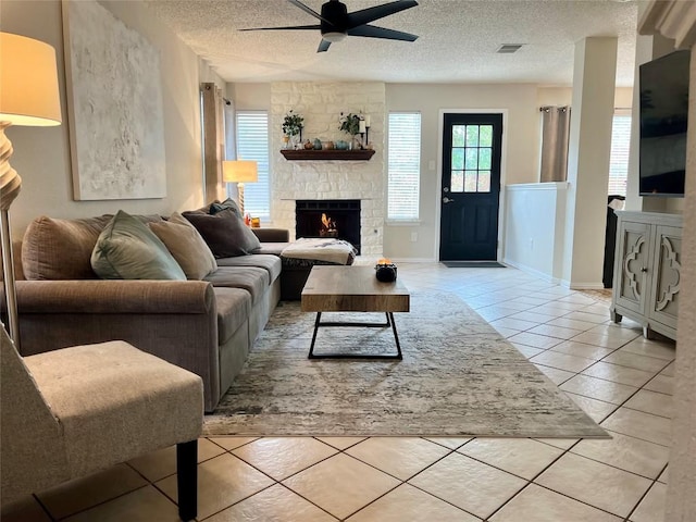 living room featuring visible vents, a fireplace, ceiling fan, a textured ceiling, and light tile patterned floors
