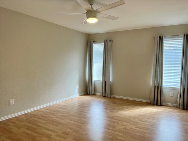 spare room featuring a ceiling fan, baseboards, a wealth of natural light, and light wood-type flooring