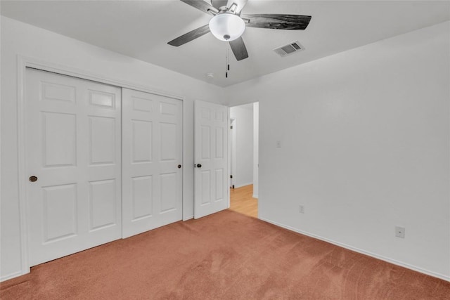 unfurnished bedroom featuring visible vents, a closet, baseboards, light colored carpet, and a ceiling fan