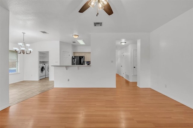 unfurnished living room with light wood-style floors, visible vents, ceiling fan with notable chandelier, and washing machine and clothes dryer