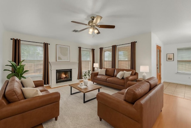 living room with ceiling fan, a glass covered fireplace, a wealth of natural light, and visible vents
