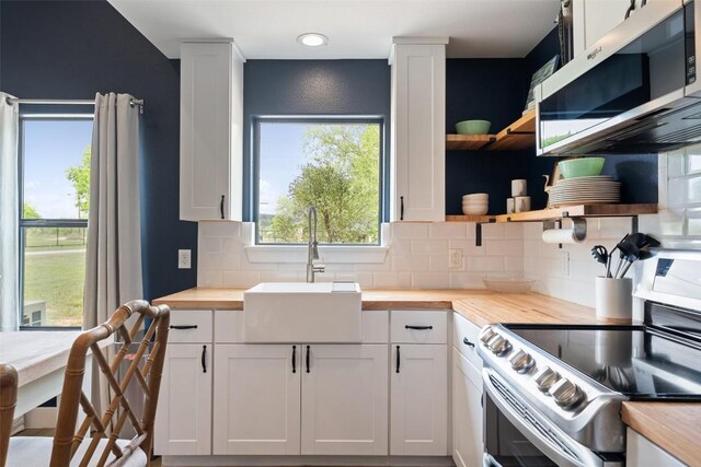 kitchen with open shelves, a sink, wood counters, stainless steel appliances, and decorative backsplash
