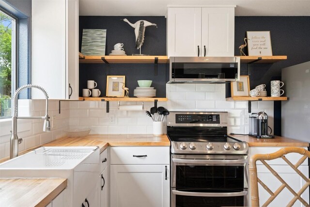 kitchen featuring open shelves, appliances with stainless steel finishes, a sink, butcher block countertops, and decorative backsplash