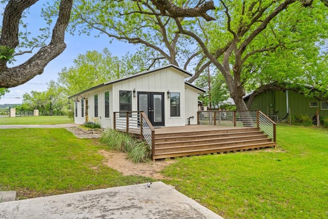 back of property with french doors, a wooden deck, board and batten siding, and a yard