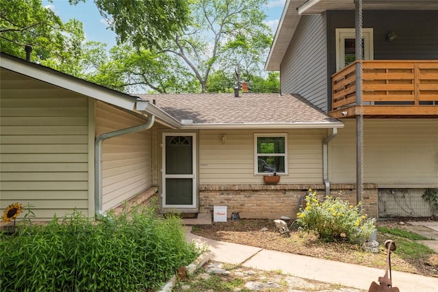 entrance to property with brick siding, a balcony, and roof with shingles